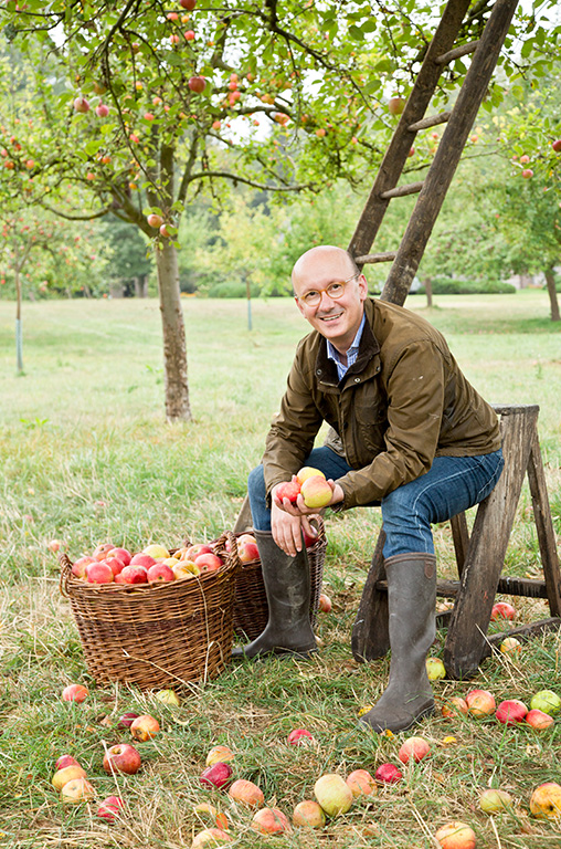 Ein Portrait-Bild von Peter van Nahmen inmitten von Äpfeln vor einem Baum.