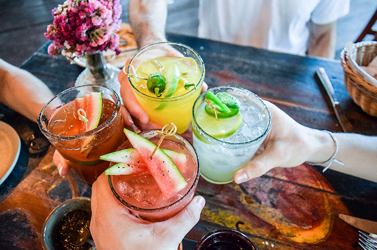 Fröhliche Menschen stoßen mit Gläsern voller verschiedener Cocktails mit Sirup an.